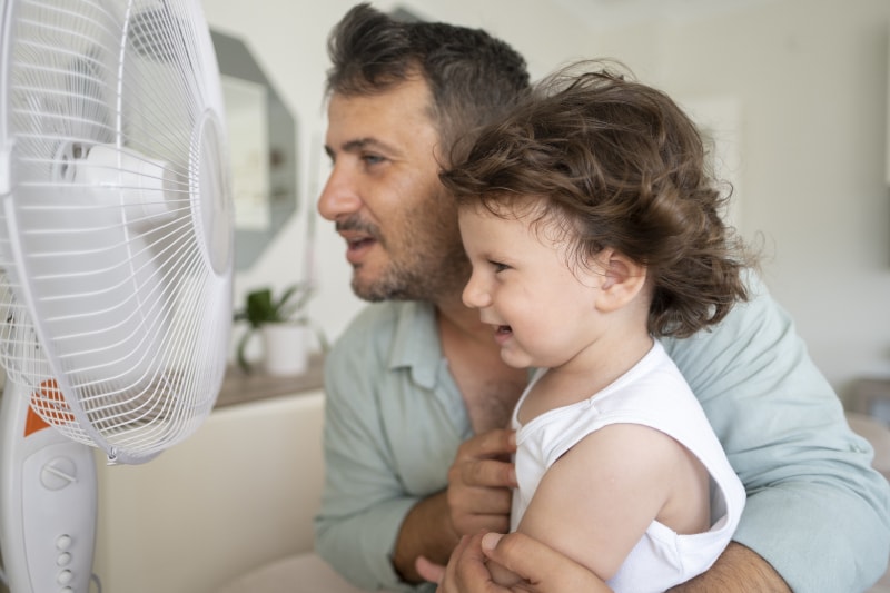 Father and daughter in front of fan trying to cool off, because they need air conditioning repair in Brunswick, OH. Gene's Heating & Air Conditioning, Plumbing & Electrical blog image.