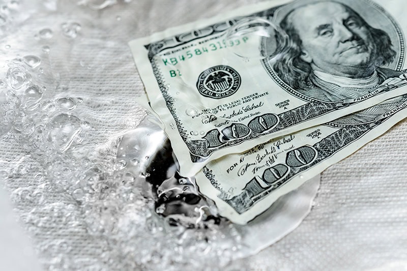 Two One Hundred dollar bills being washed down the drain.