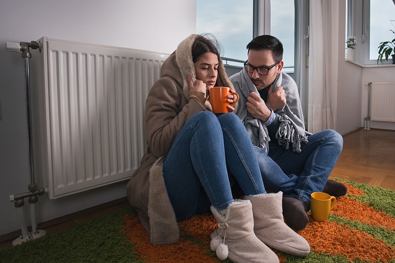 Couple next to furnace with blanket wrapped around them.