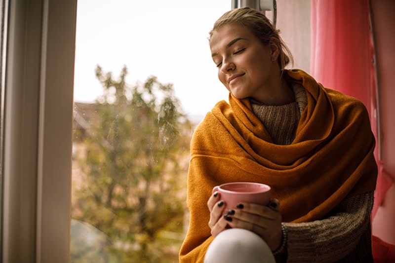 Woman sitting against a window looking cozy, fall background.
