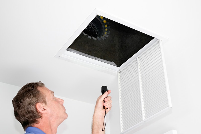 Man looking into air duct with a flashlight.