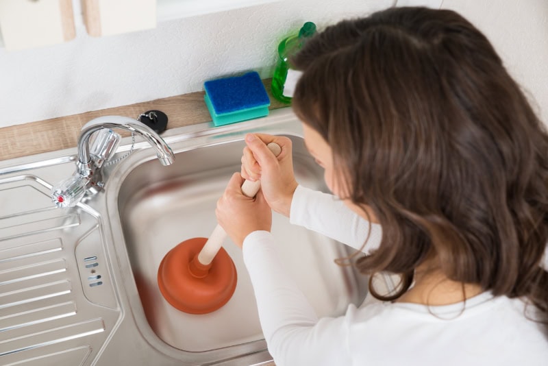 Woman Using Plumbing To Unclog Sink