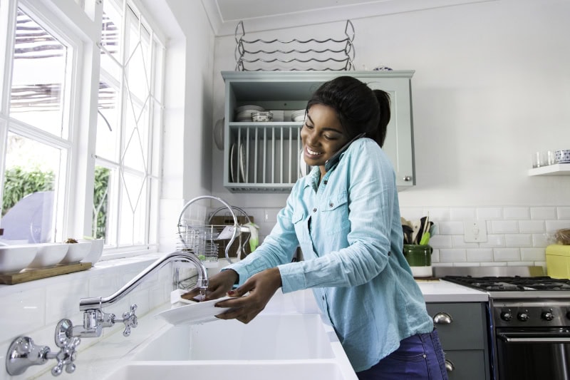 Why Is My Garbage Disposal Humming? African female doing the dishes while having a conversation on her mobile phone, laughing. Cape Town, Western Cape, South Africa.