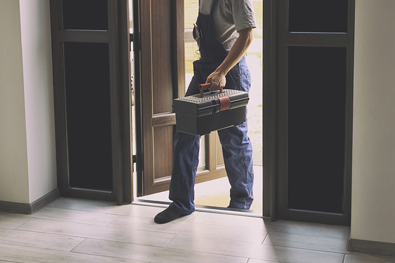 HVAC technician walking into home with a toolbox.