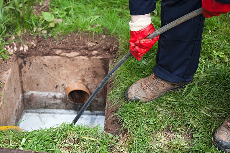 How Often Should I Clean My Sewer Line? Photo of a plumber performing maintenance on a sewer line under ground.